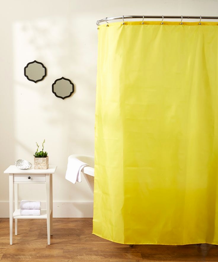 Bright yellow shower curtain in a minimalist white bathroom with a small side table and soft daylight