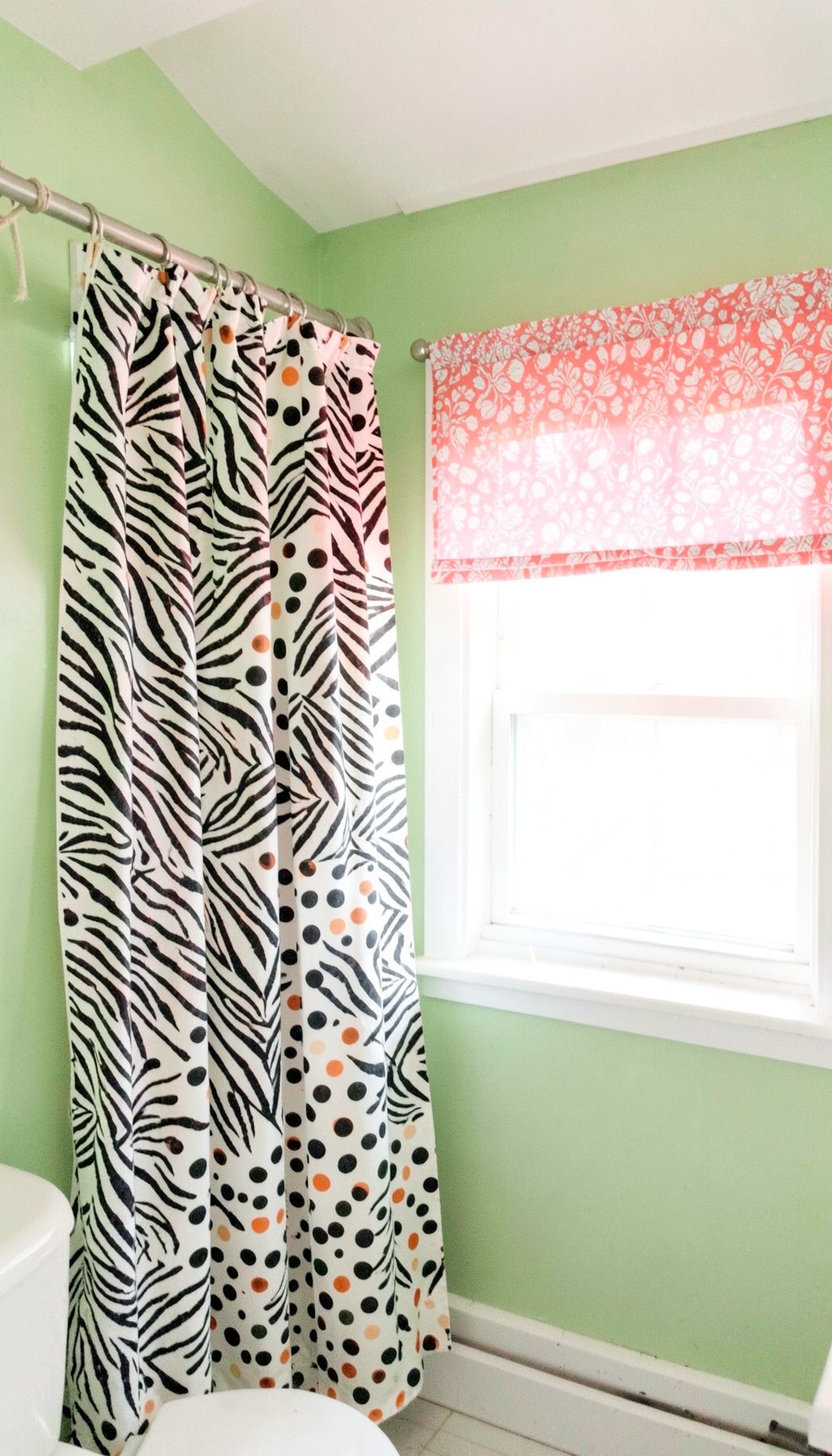 Bathroom with green walls, a zebra print and polka dot curtain and a pink patterned window valance