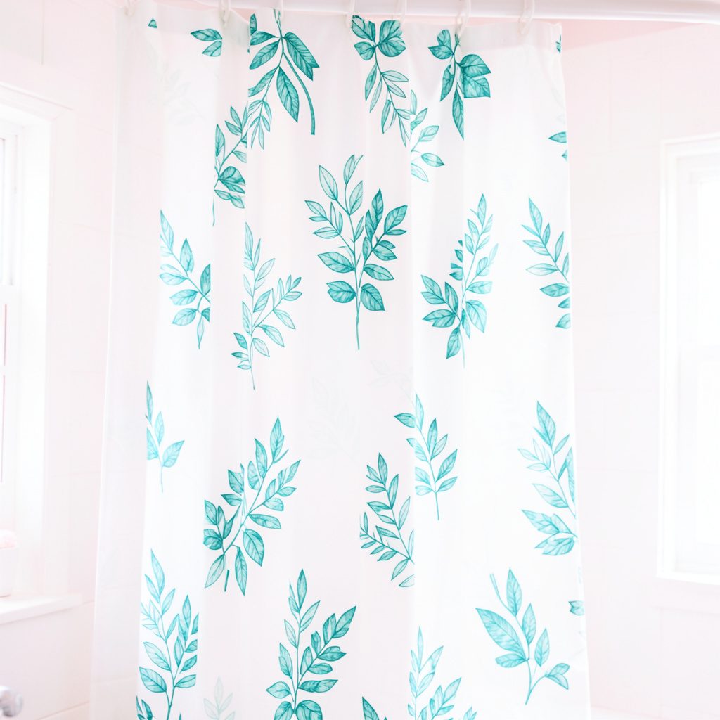 Bright high-key photograph of a white textile decorated with teal and green leaf patterns, hanging softly in even daylight